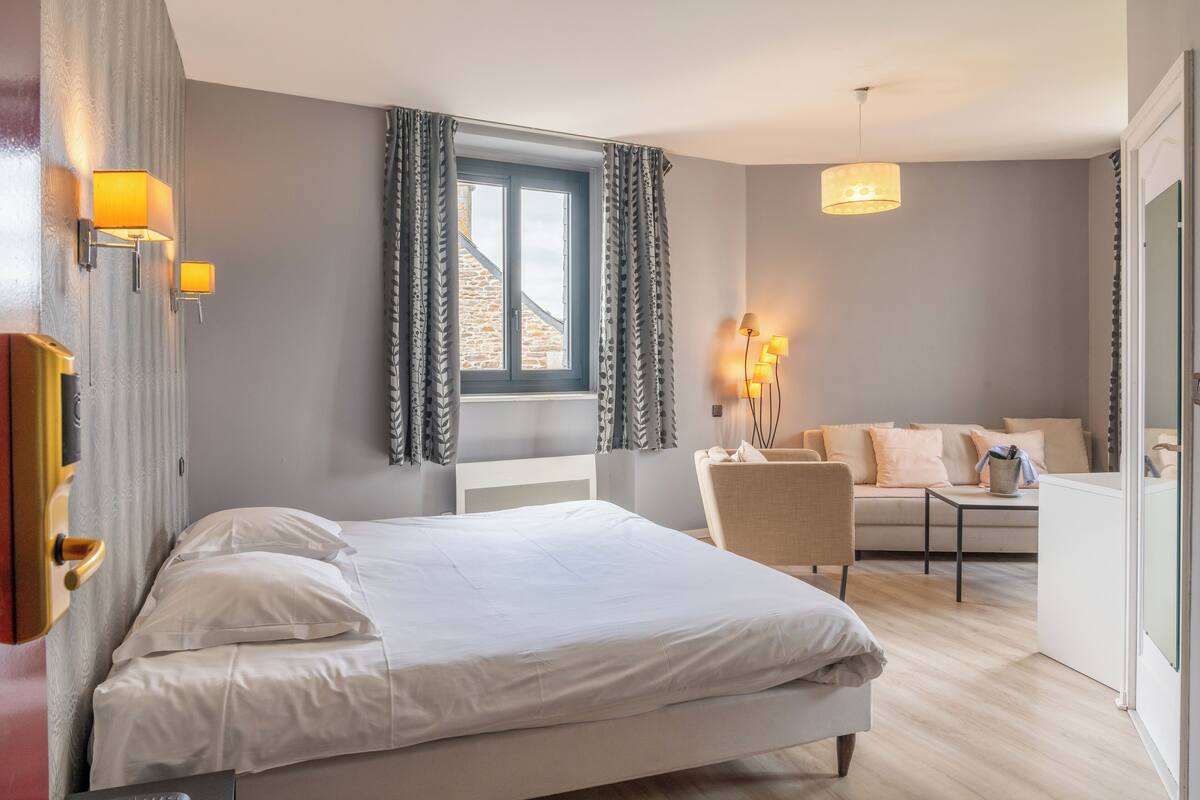 Un dormitorio con cama, una silla, un sofá y una ventana con cortinas.