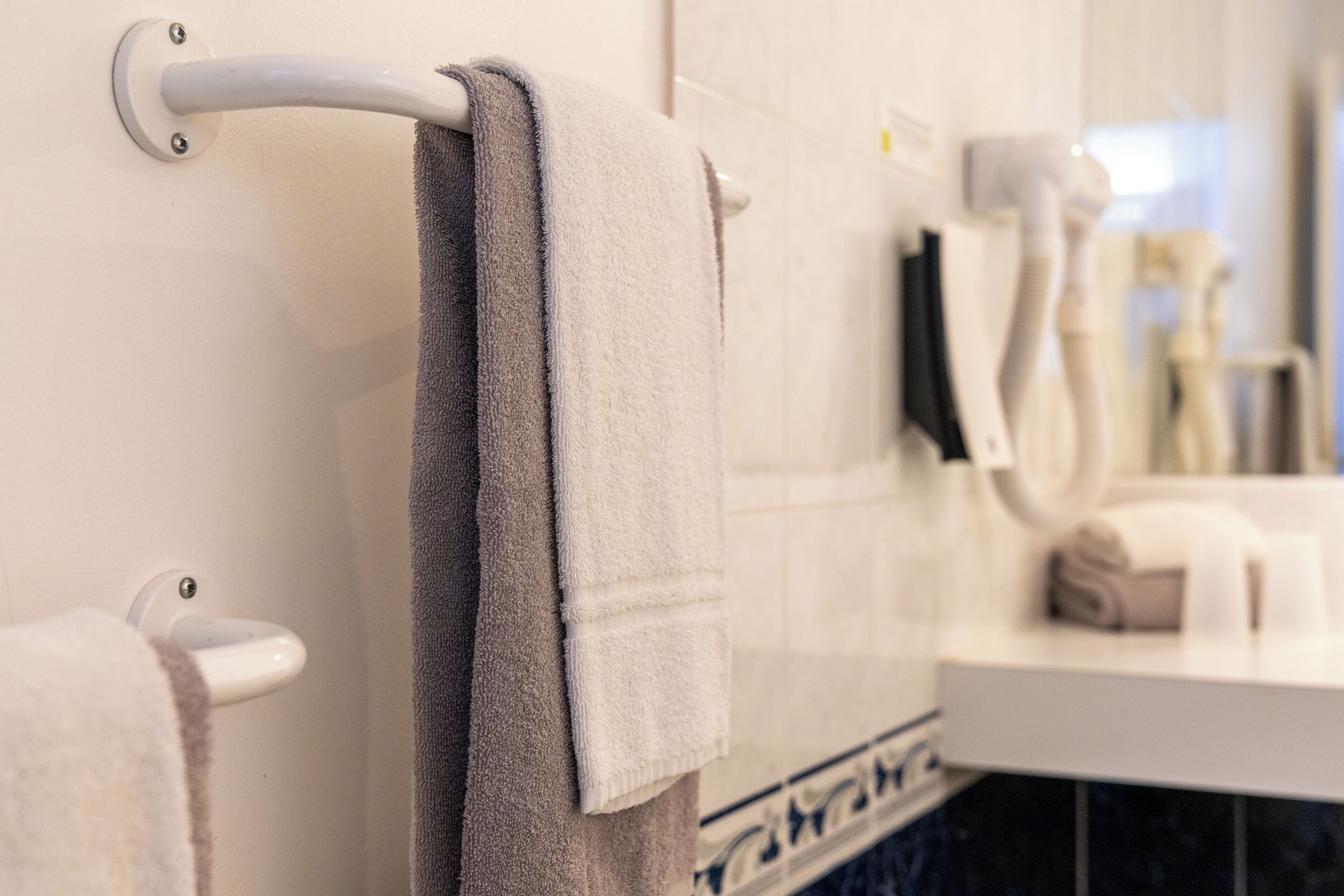 Un baño con un perchero que sostiene dos toallas, un lavamanos blanco y un espejo.