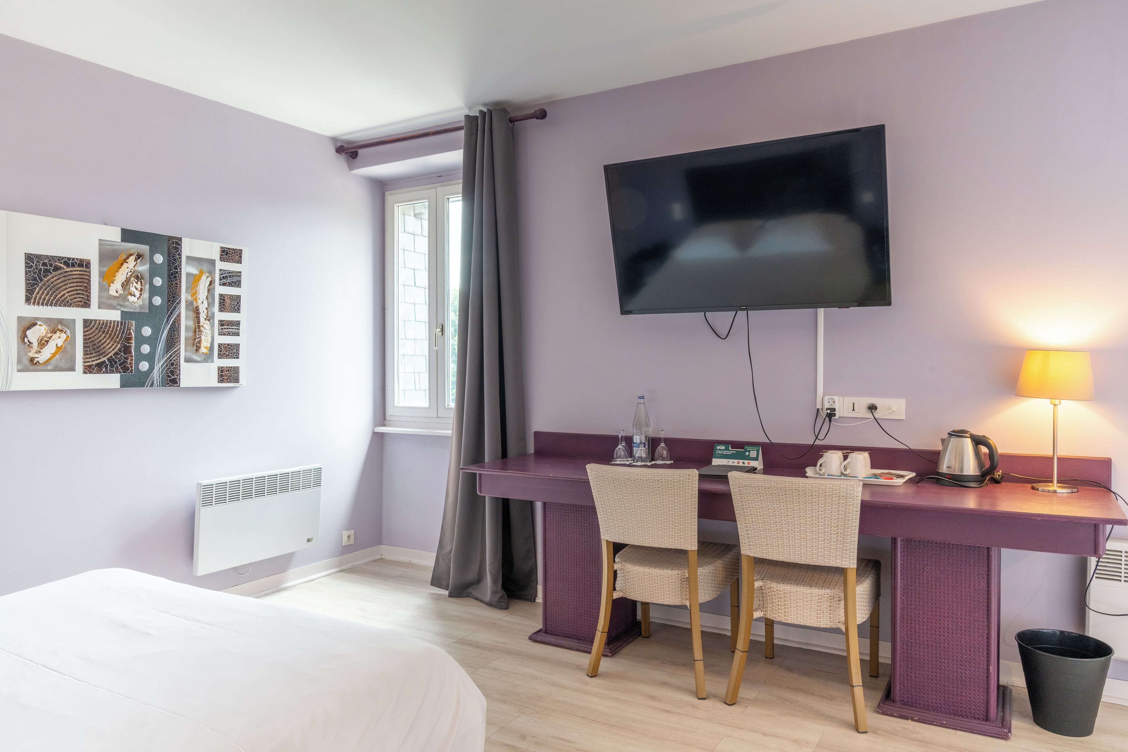 Ein Hotelzimmer mit einem Bett, einem Schreibtisch mit zwei Stühlen, einem Flachbildfernseher, einer Lampe und einem Wandbild.