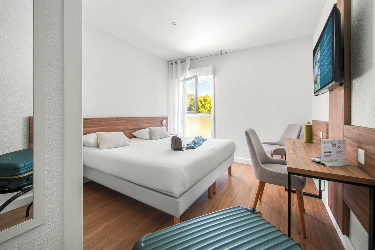 A hotel room with a bed, a desk, a chair, and a view of the outdoors.