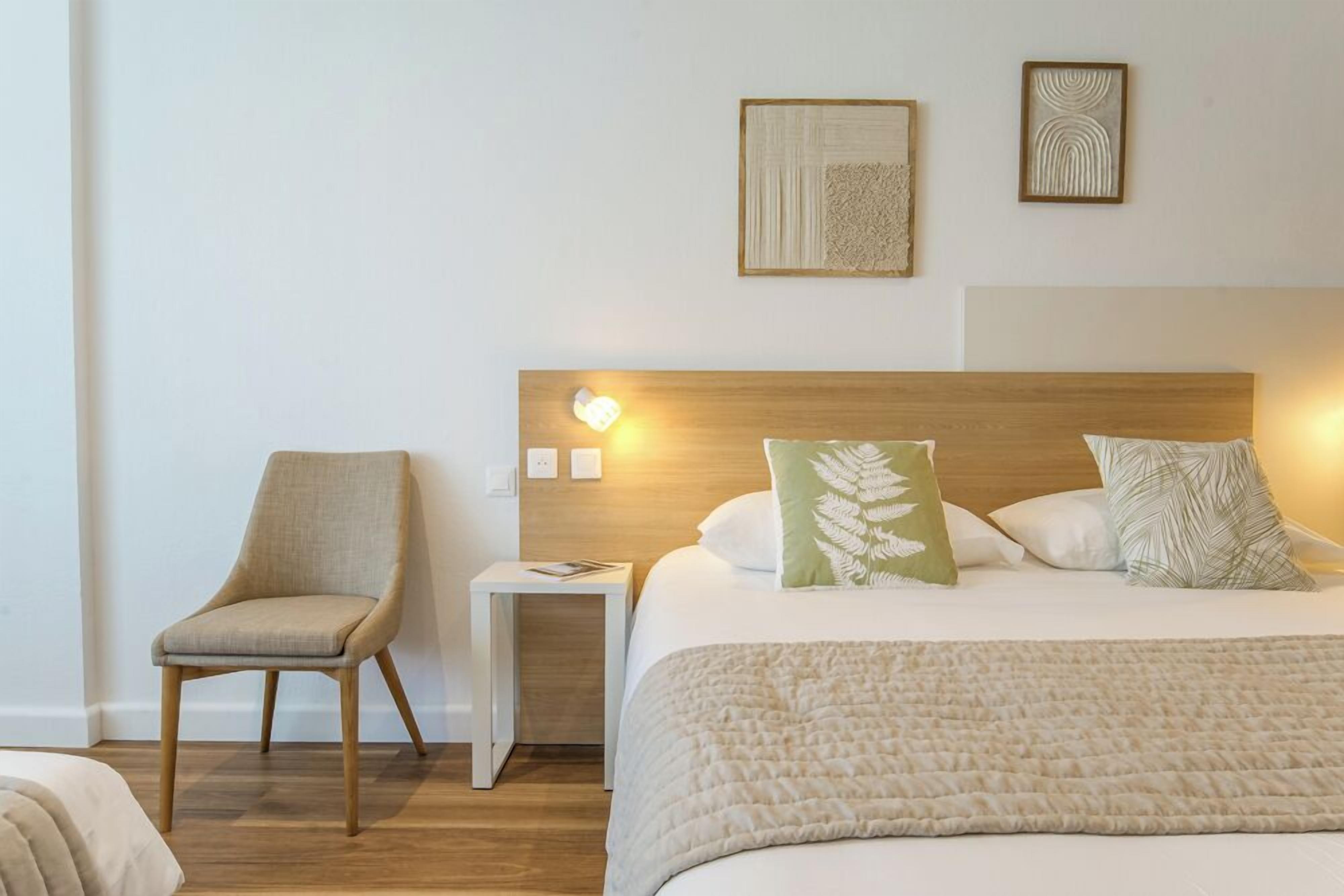 A hotel room with a bed, a chair, a nightstand, and two wall-mounted artworks.