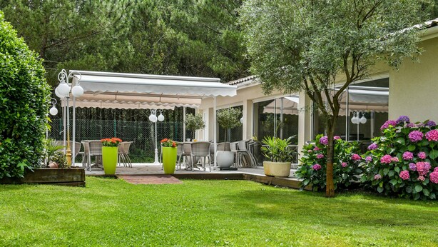A covered patio area with outdoor furniture, a pergola, and a garden with hydrangeas. - Hotel La Forestière (Biscarrosse)