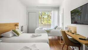 A hotel room with two beds, a desk, a chair, a TV, and a window with a view of greenery. - Hotel La Forestière (Biscarrosse)