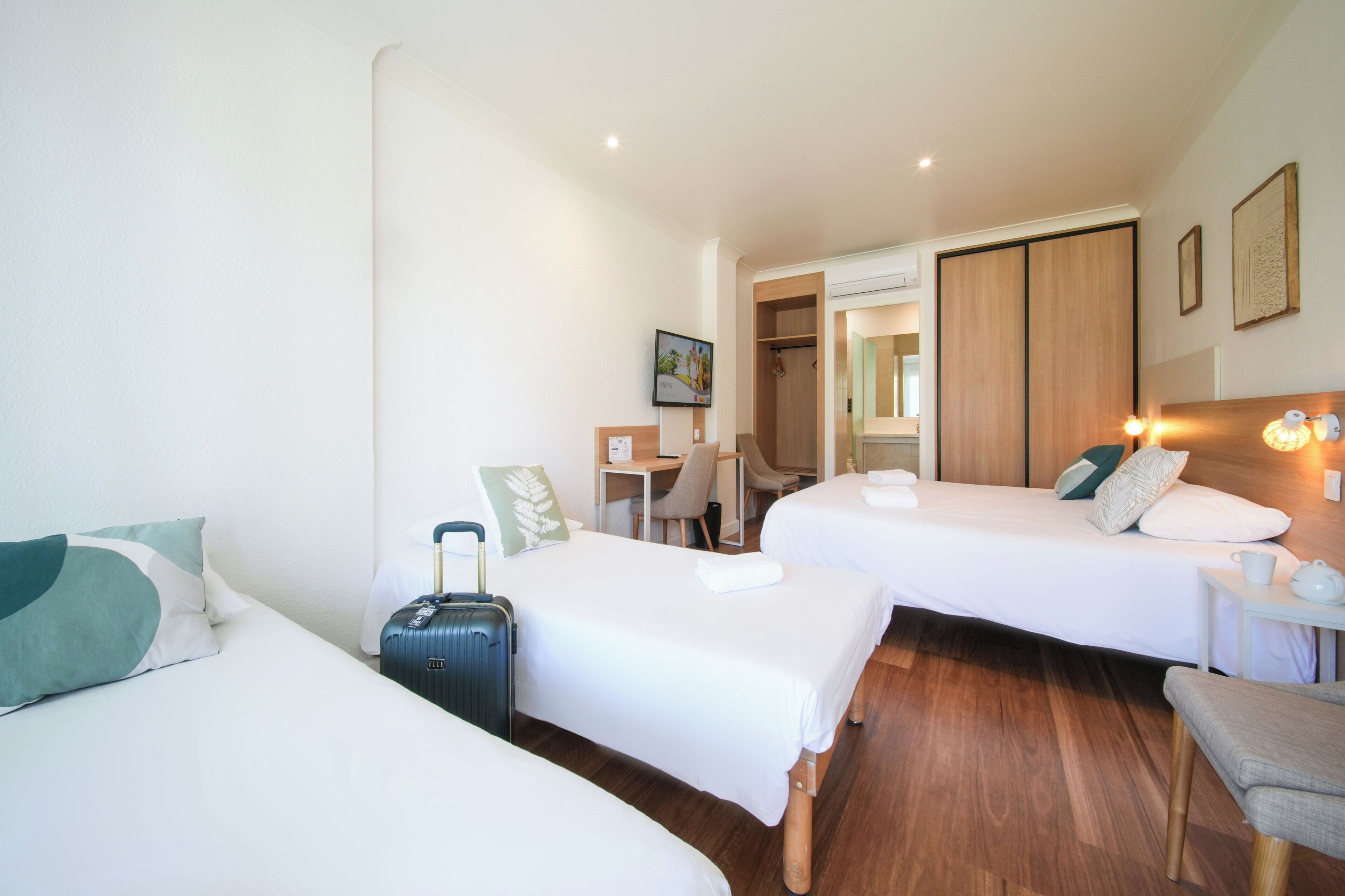 Habitación de hotel con dos camas, un escritorio, una silla, una maleta y una mesita de noche con lámpara.
