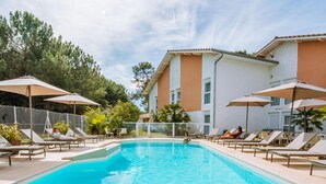 A swimming pool with lounge chairs and umbrellas, surrounded by a fence and trees. - Hotel La Forestière (Biscarrosse)