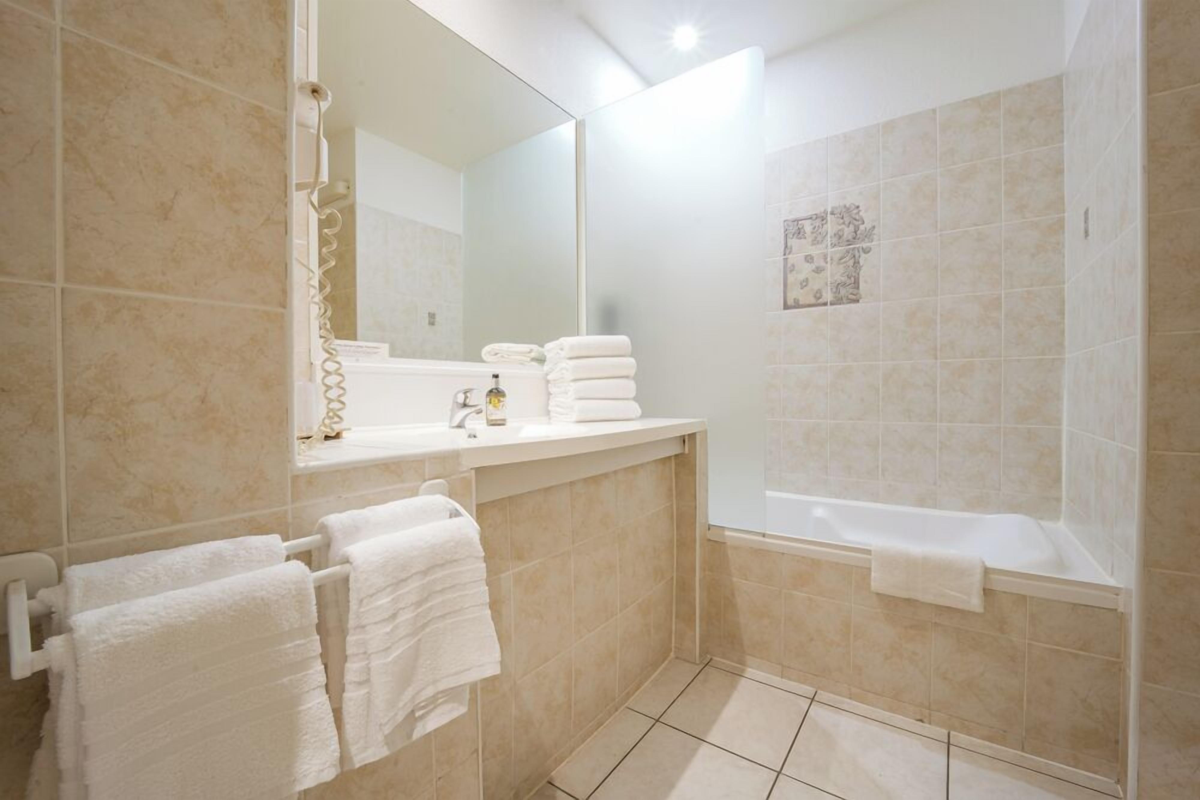 Un baño con bañera, lavamanos con espejo y toallero.