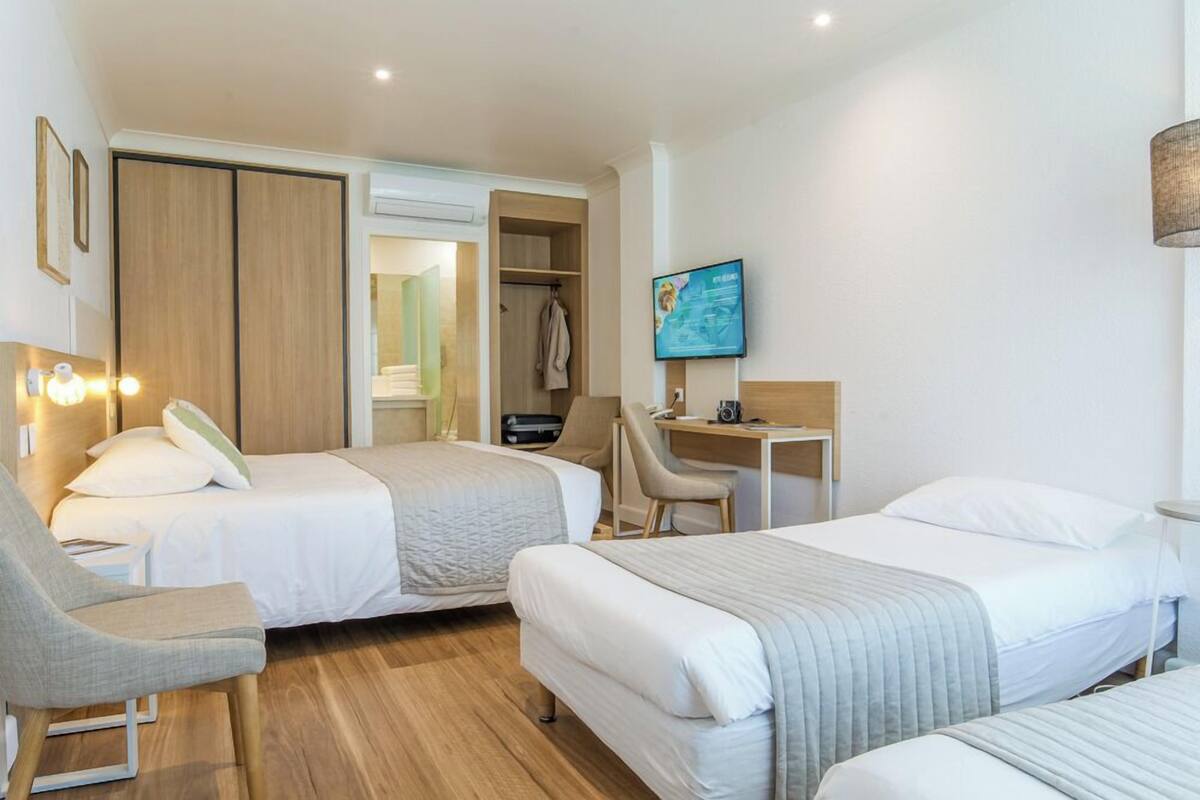 A hotel room with two beds, a desk, a chair, a wardrobe, and a television.