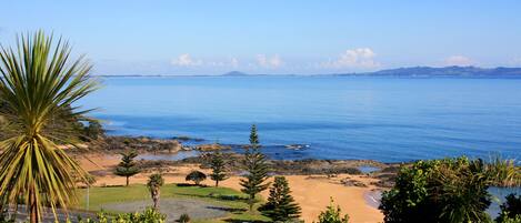 A coastal landscape with a sandy beach, rocky outcrops, and a clear blue sea.