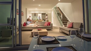 A modern living room with a glass partition, a dining area with a table set for two, and a staircase leading to an upper floor. - Doubtless Bay Villas (Cable Bay)