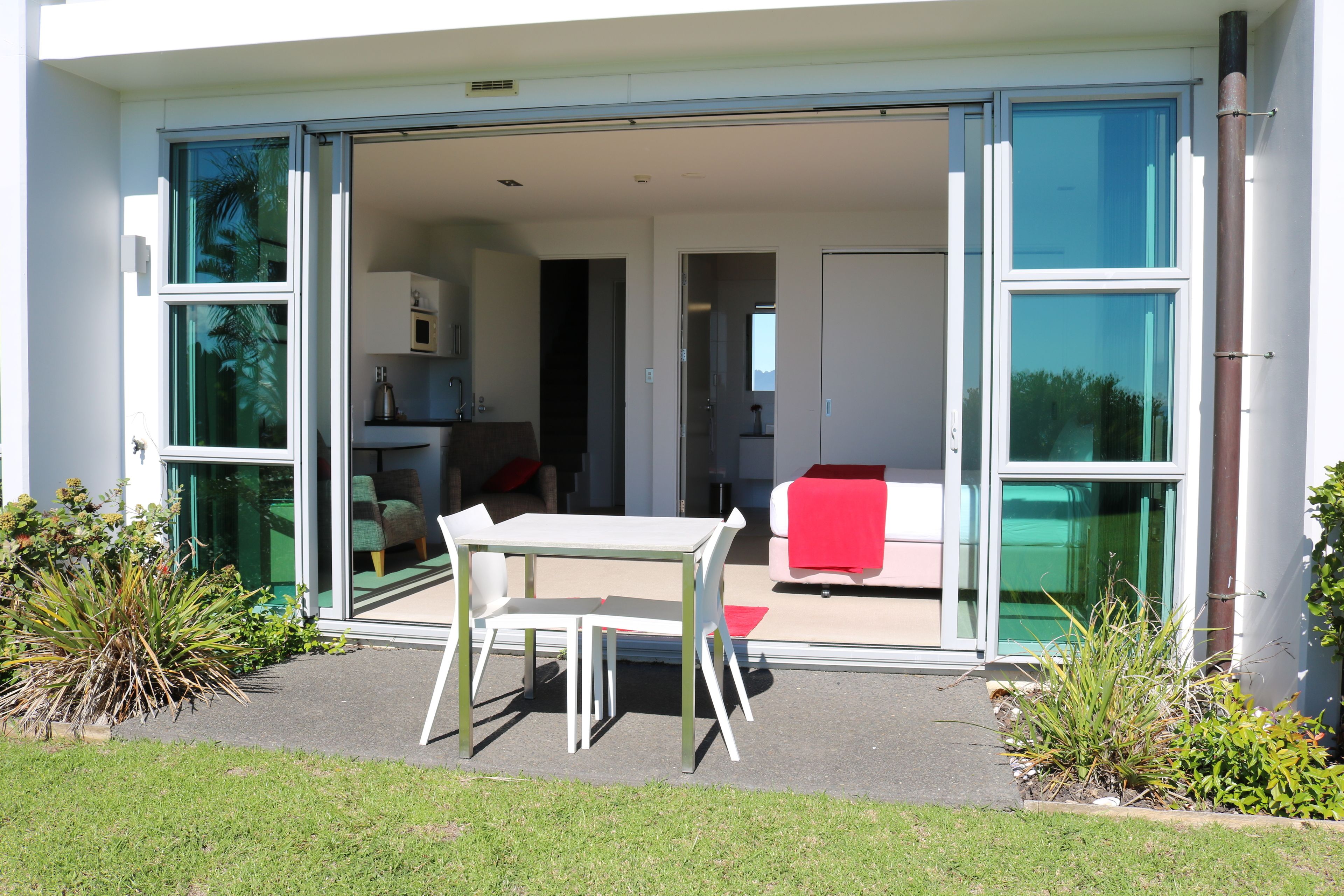Une maison moderne avec une porte vitrée donnant sur un patio agrémenté d’une table et de chaises blanches.