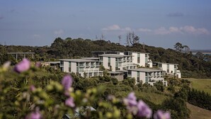 A modern multi-story building with a flat roof, surrounded by lush greenery and hills. - Doubtless Bay Villas (Cable Bay)