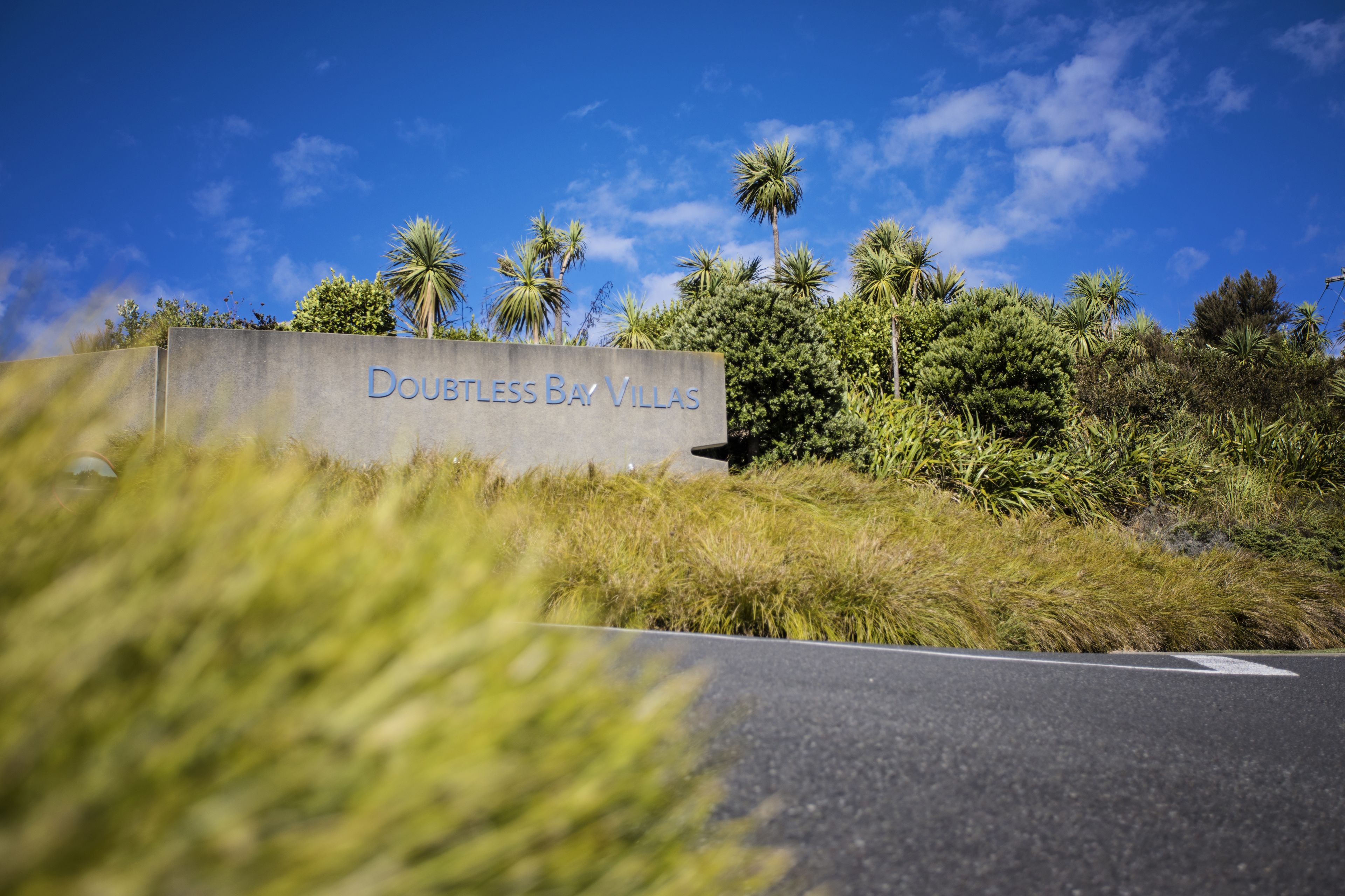 A sign for Doubtless Bay Villas with a clear sky and palm trees in the background.