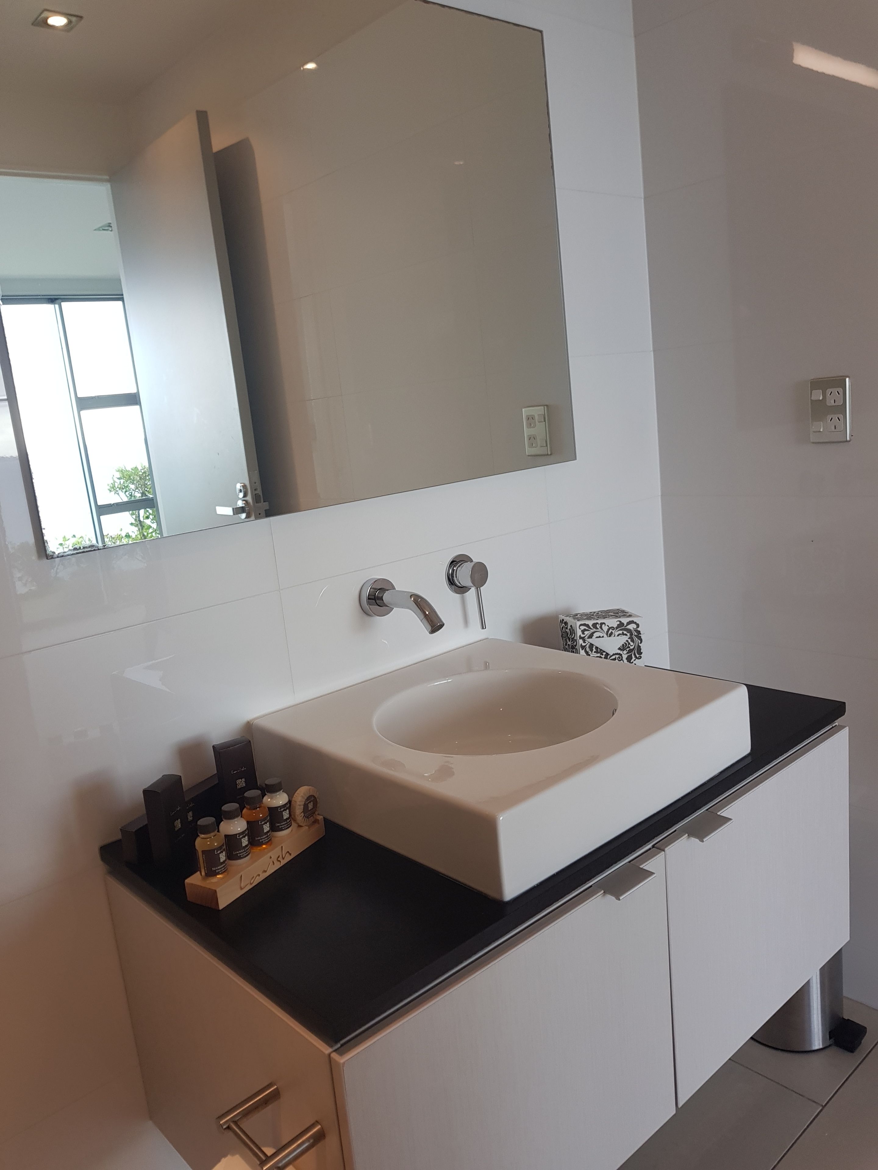 A modern bathroom with a large mirror, a white sink, and a black countertop.
