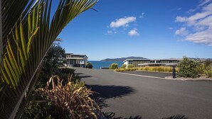A modern building with a curved driveway, surrounded by tropical plants and a clear view of the ocean. - Doubtless Bay Villas (Cable Bay)