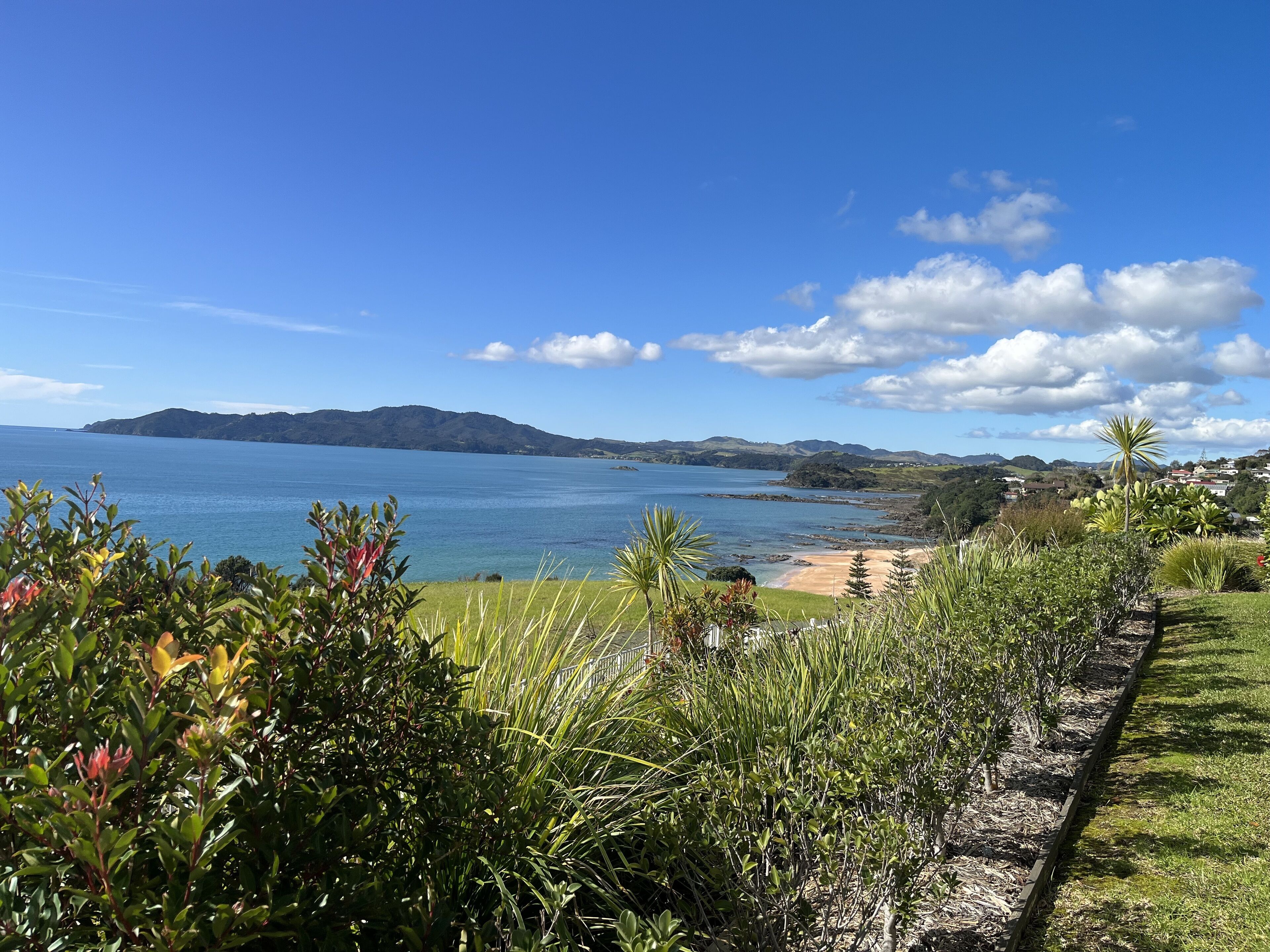 A coastal landscape with a clear view of the sea, a sandy beach, and distant hills.