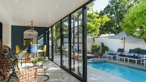 Un área de piscina interior moderna con paredes de vidrio, mobiliario de mimbre y un comedor con sillas amarillas.