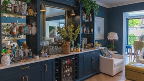Zona de bar con estantes llenos de botellas, un refrigerador y un área de descanso con un sillón y reposapiés.