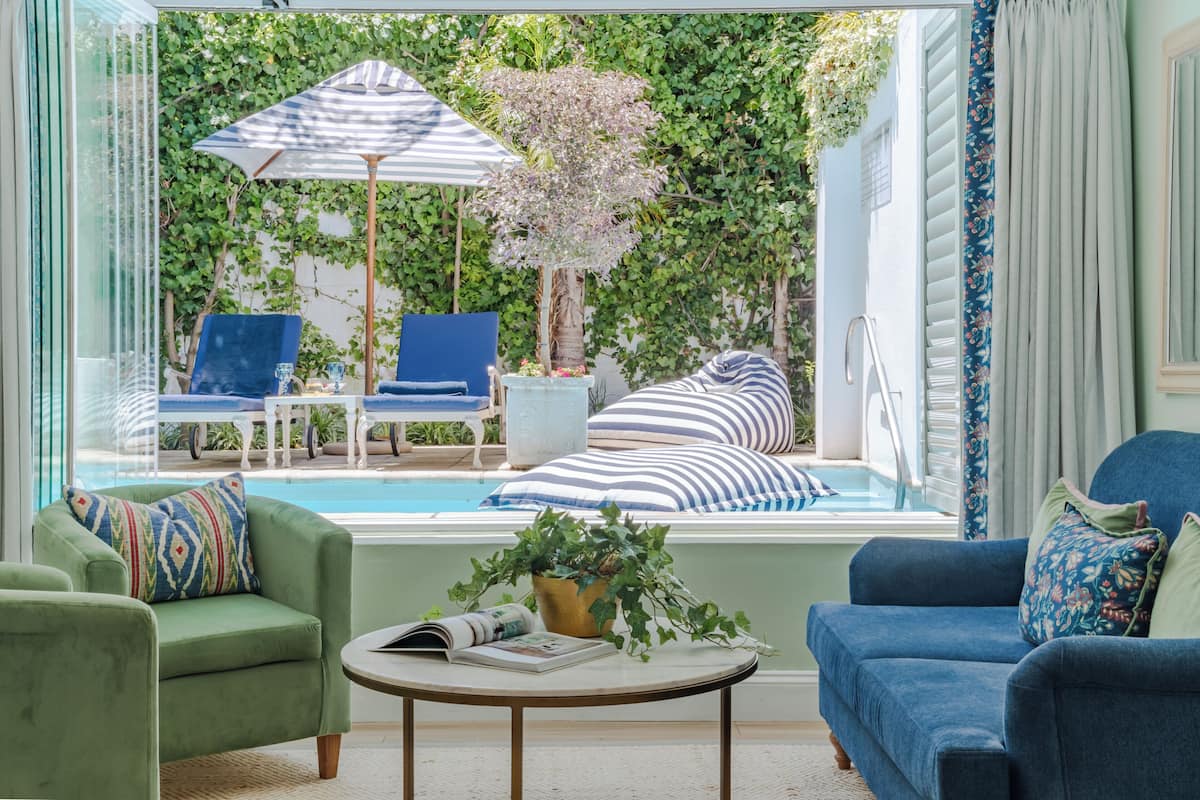 A room with a view of a pool, a blue chair, a green armchair, and a striped sofa.