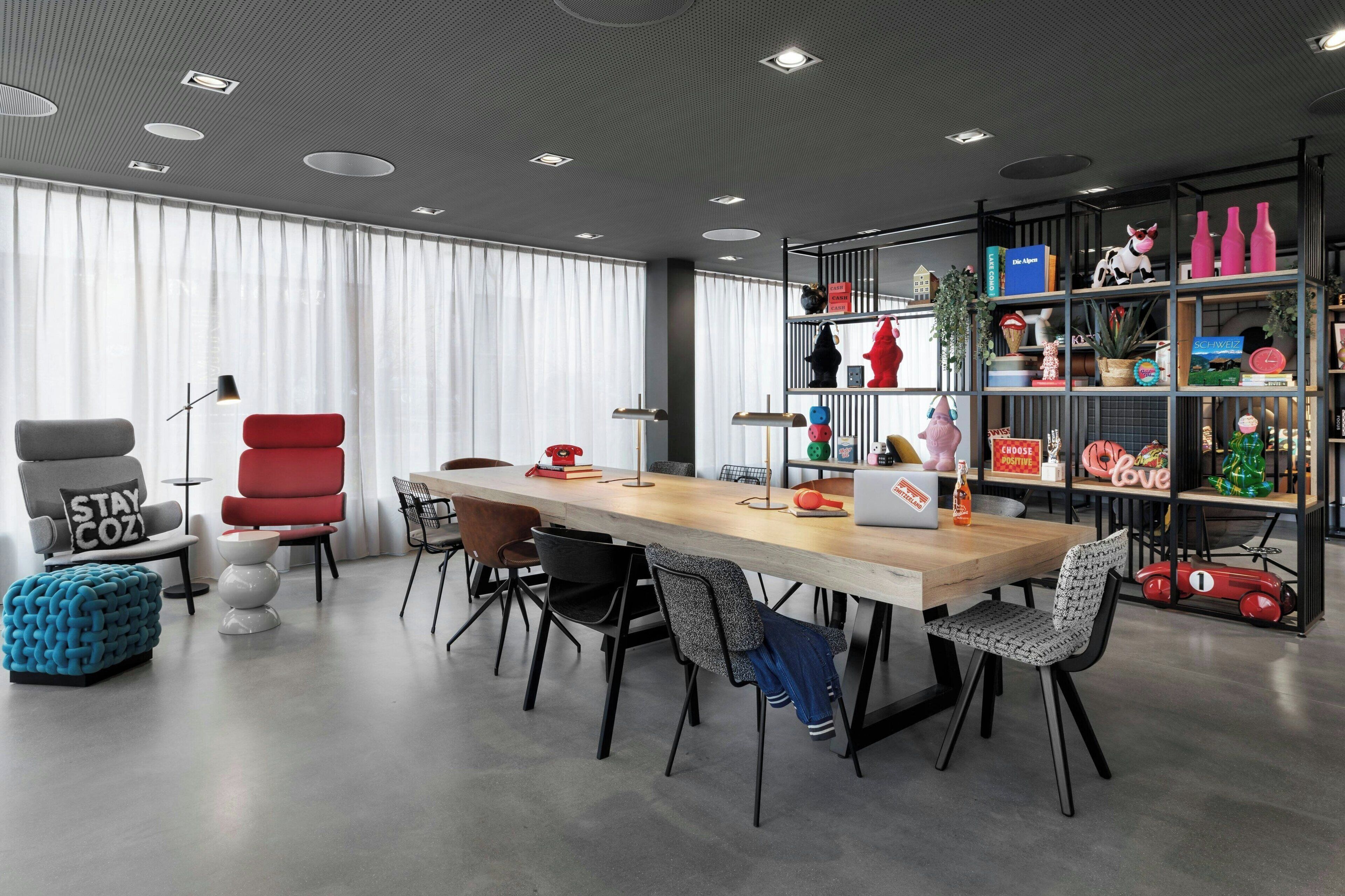 Una moderna sala da pranzo con un lungo tavolo di legno, sedie nere e rosse e una libreria piena di oggetti diversi.