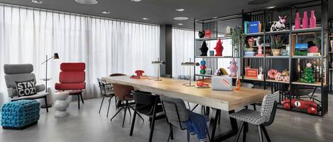 A modern dining area with a long wooden table, black and red chairs, and a bookshelf filled with various items.