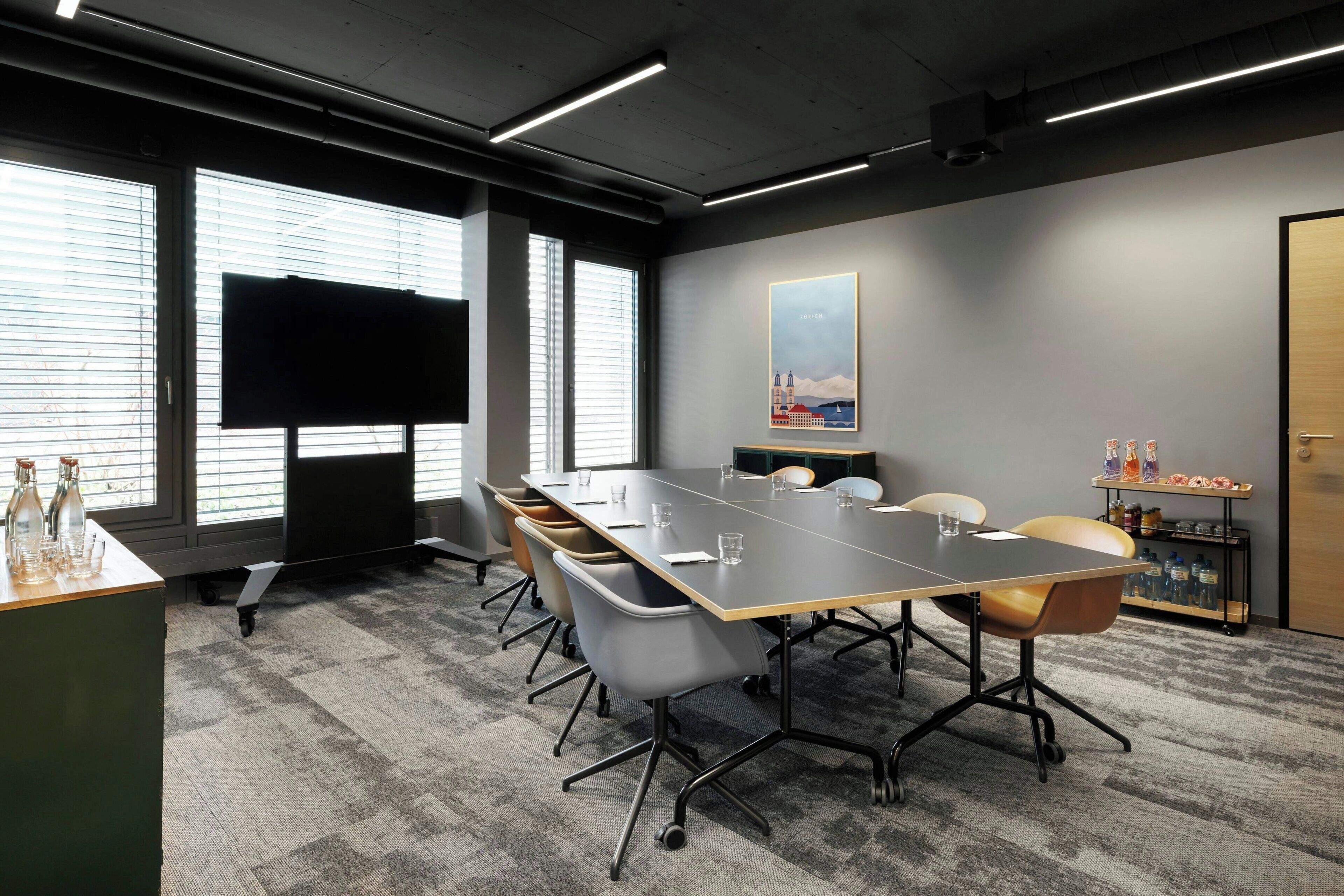 A conference room with a long table, chairs, a projector screen, and a large window with blinds.