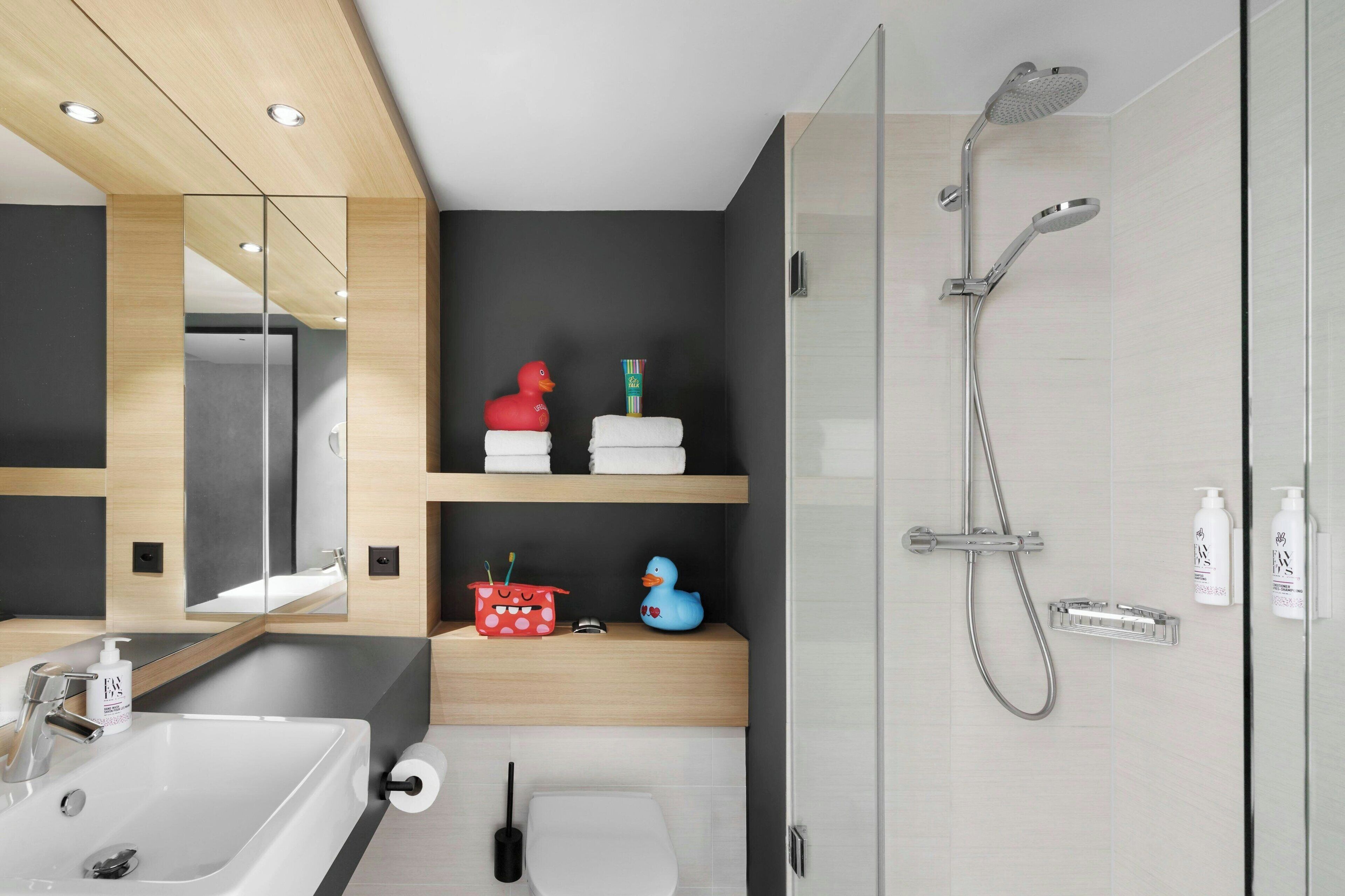 Un bagno moderno con un ampio specchio, due lavabi, una doccia e oggetti decorativi come paperelle di gomma.