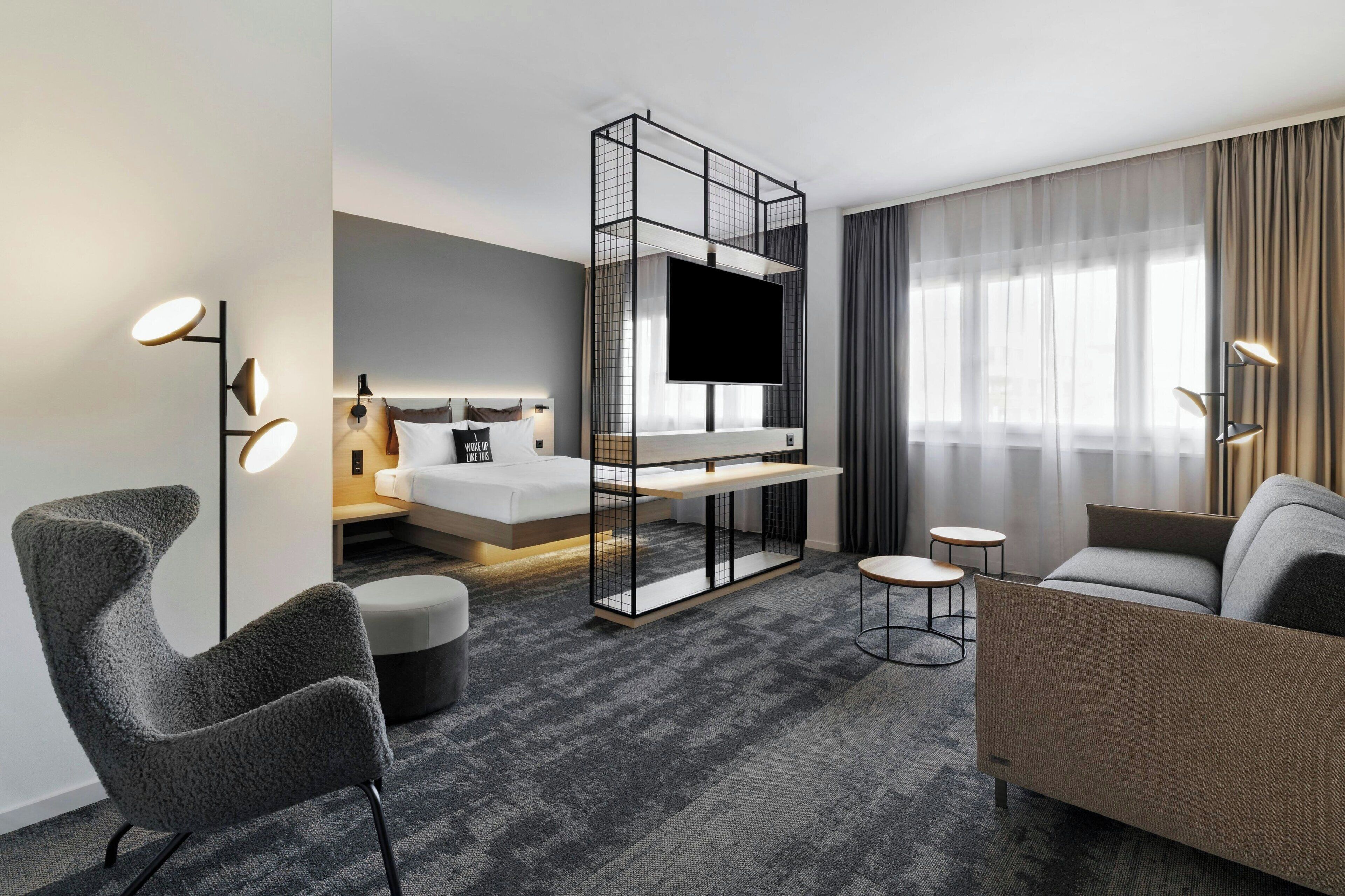A modern hotel room with a bed, a TV, a sofa, and a desk.