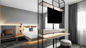 A modern hotel room with a bed, a TV mounted on a wall, a sofa, and a small table. - Moxy Zurich (Zürich)