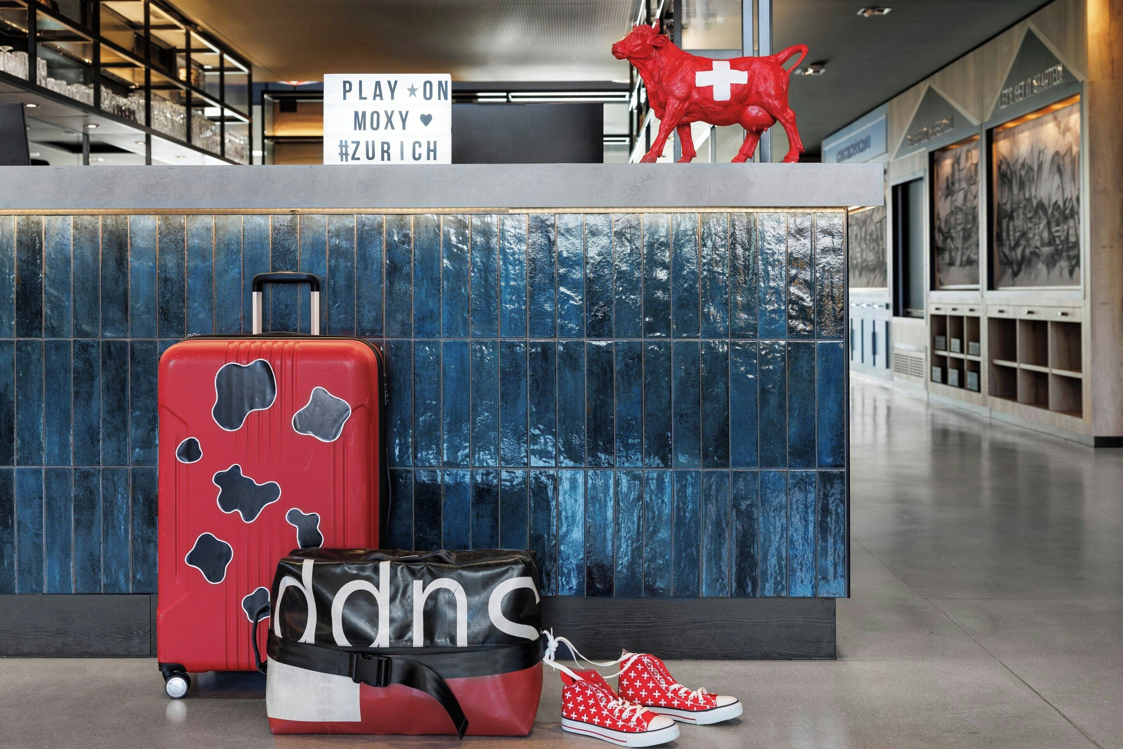 A reception desk with a red suitcase, a black and white duffel bag, and red sneakers.