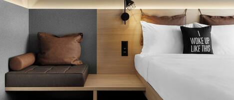 Una habitación de hotel moderna con cama, un pequeño sofá, una mesita de noche y una lámpara de pared.