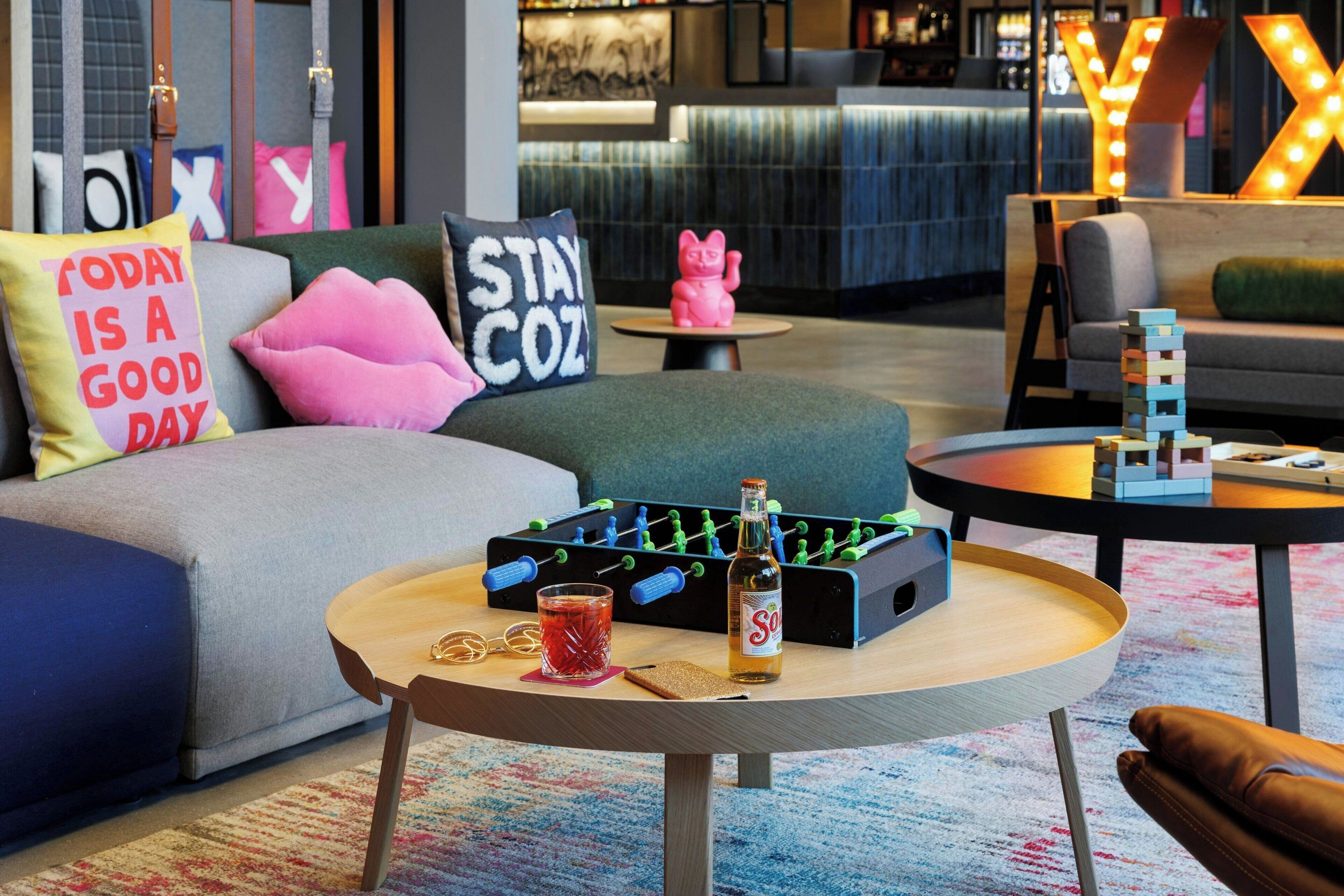 A modern lounge area with a foosball table, a bottle of soda, and a glass of red drink on a round table.