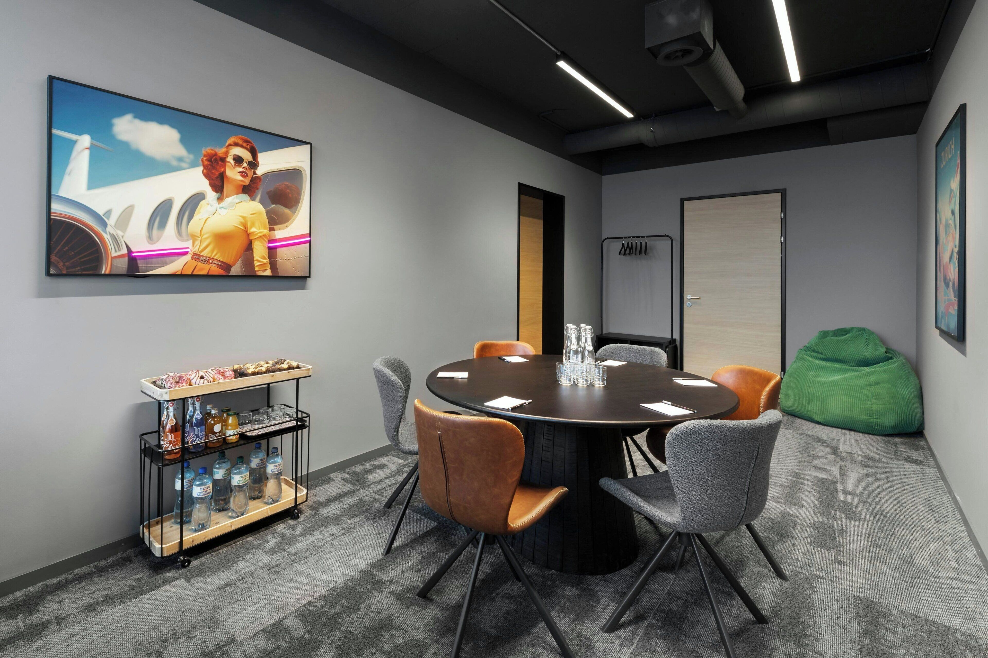A conference room with a round table, grey chairs, a beverage cart, and a painting of a woman in a yellow dress.