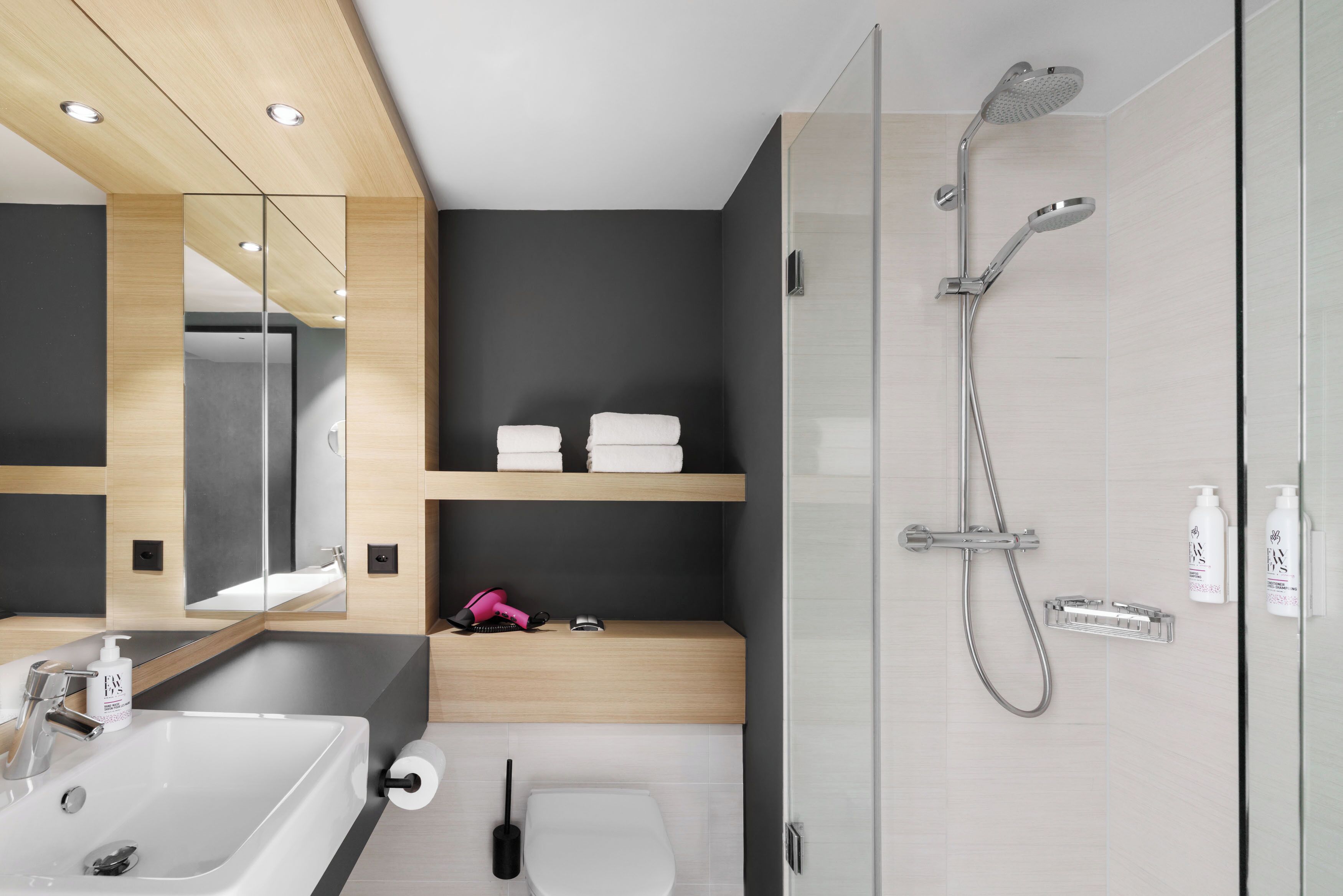 Een moderne badkamer met een douche met glazen wand, een wastafel, toilet en spiegel.