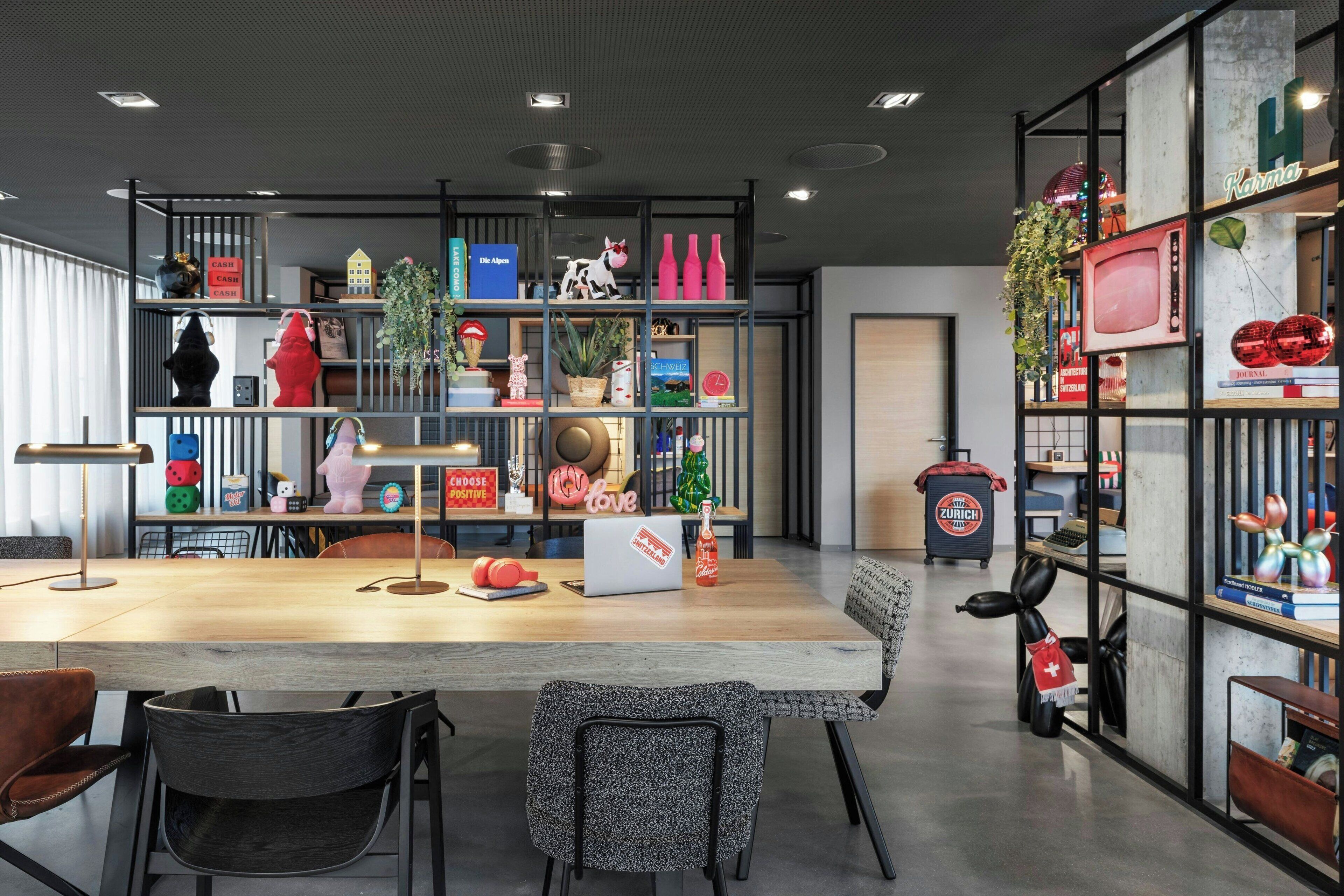 A modern interior with a wooden table, chairs, and shelves with various items including a laptop, books, and decorative objects.