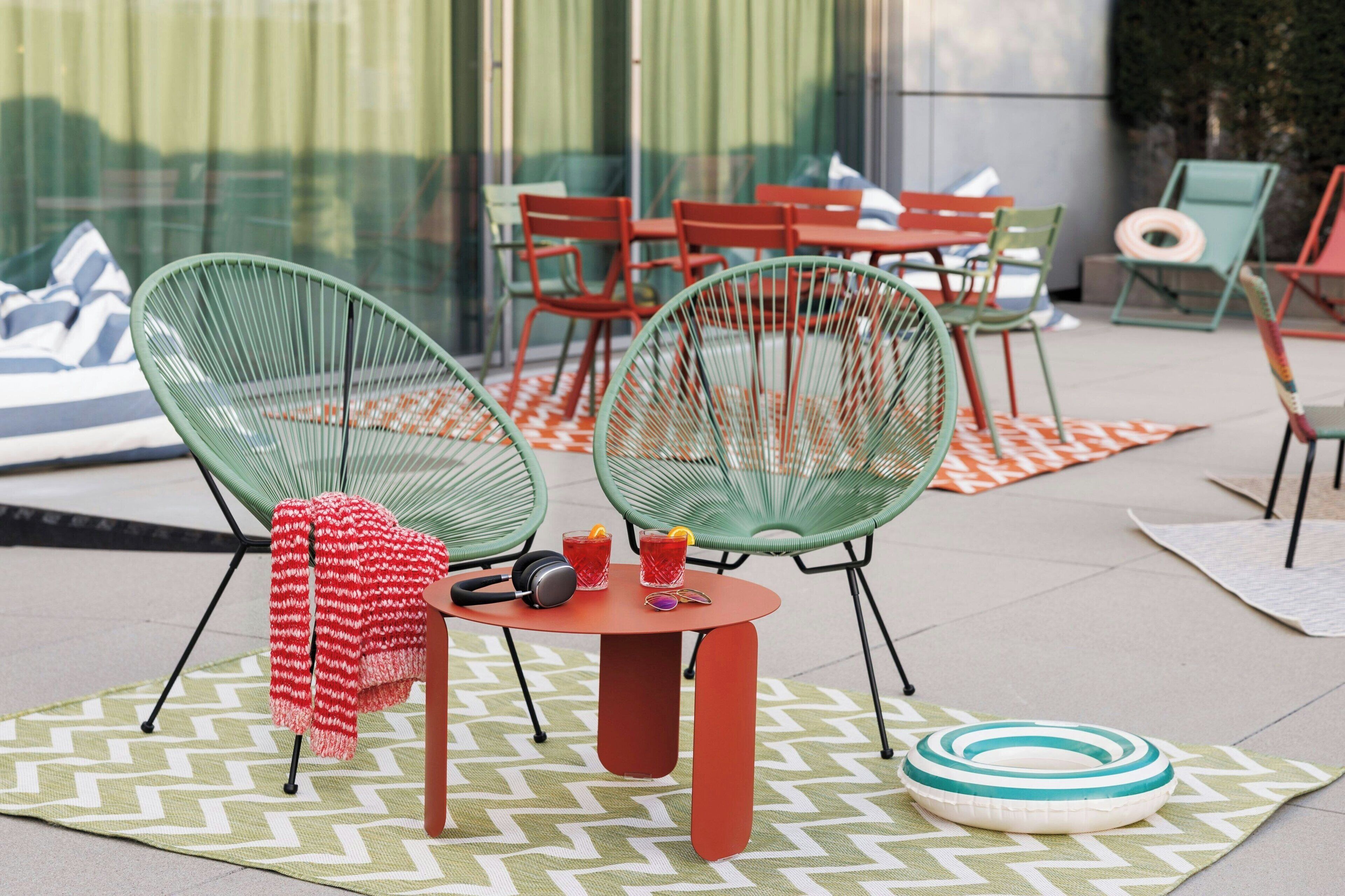 An outdoor seating area with green chairs, a red table, and a patterned rug.