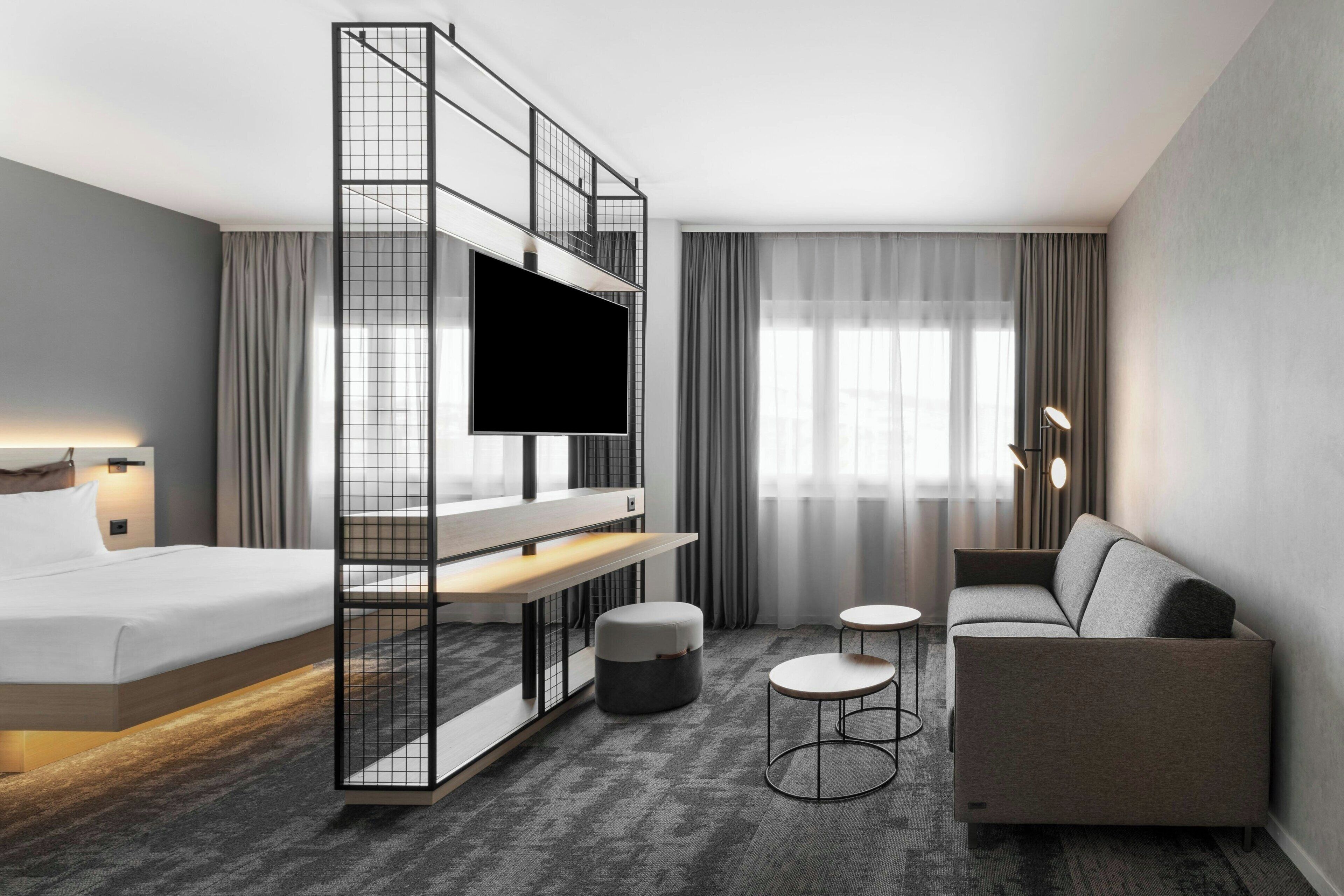 Et moderne hotelværelse med en seng, fjernsyn, sofa og et lille bord.