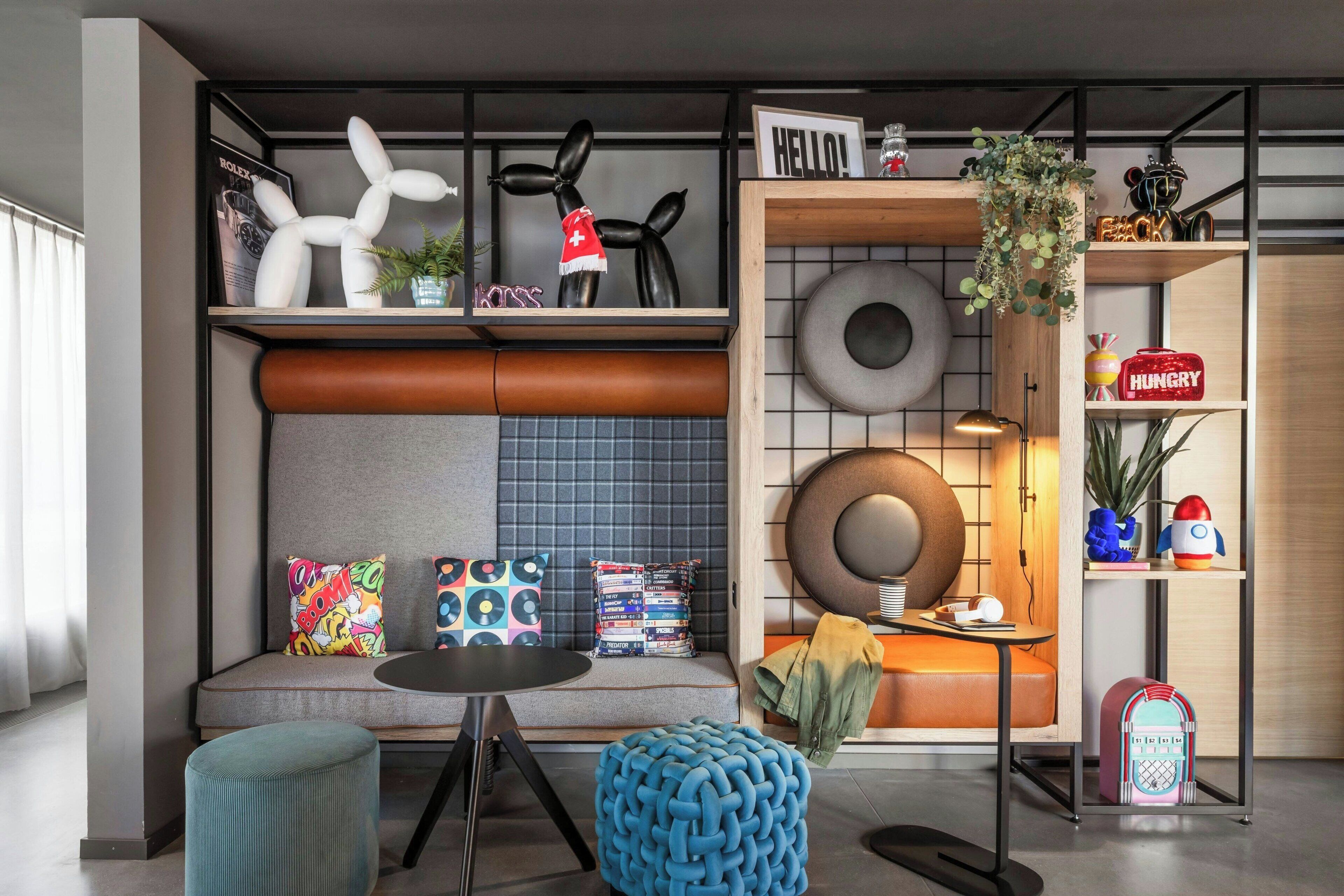 Ein modernes Wohnzimmer mit einer Couch, einem runden Tisch und einem blauen Hocker. Regale mit verschiedenen Dekorationselementen und ein Schild mit der Aufschrift "HELLO!".