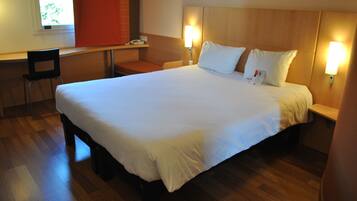 A hotel room with a large bed, a desk, and two bedside lamps.