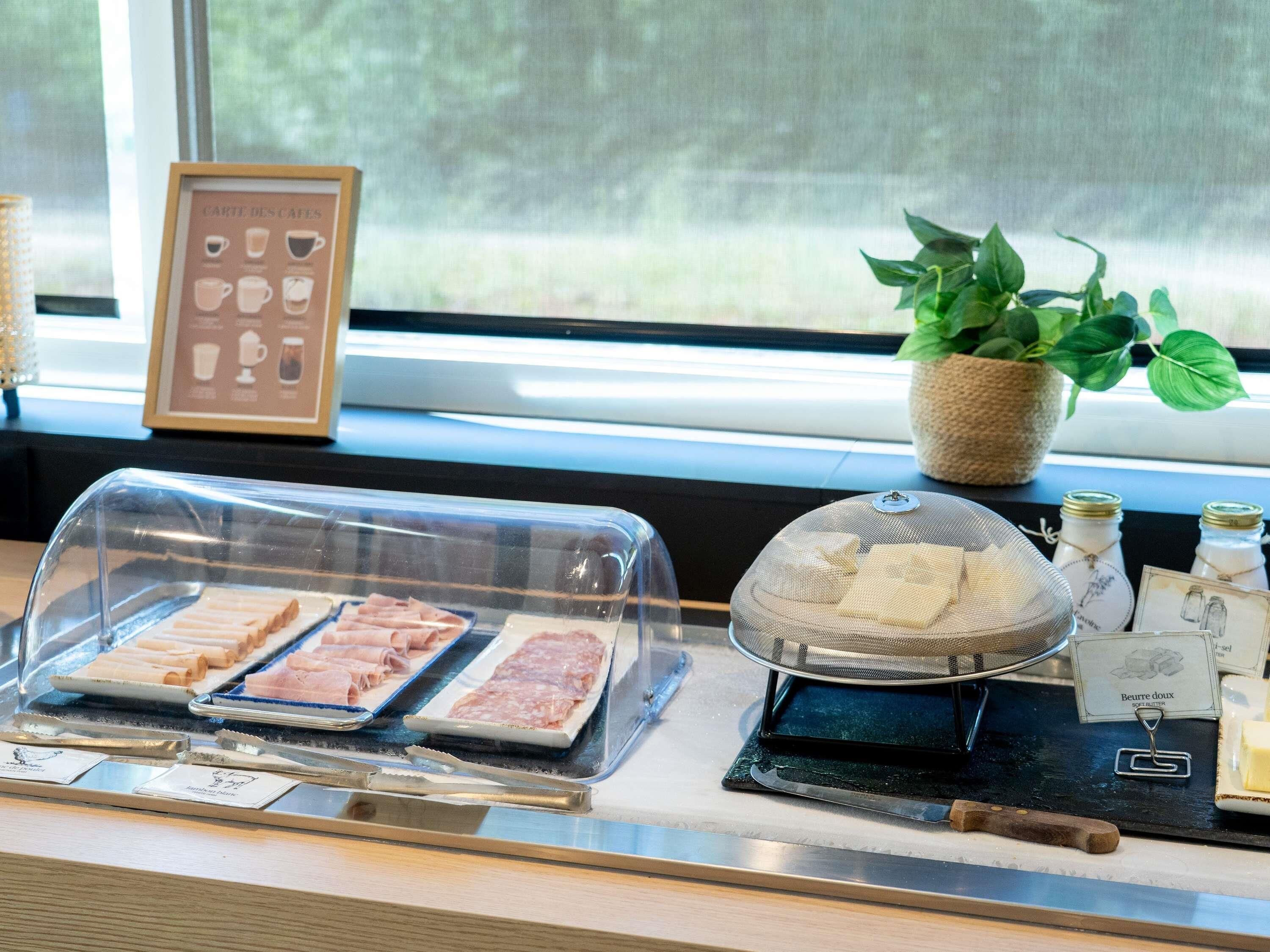 Un comptoir où l’on sert le petit-déjeuner, avec un assortiment de viandes, une plante et un panneau indiquant « Beurre doux ».