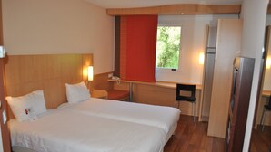 A hotel room with a large bed, a desk, a chair, and a refrigerator. - ibis Loriol Le Pouzin (Le Pouzin)