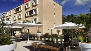 An outdoor area with a building labeled "ibis HOTEL" featuring outdoor seating and umbrellas. - ibis Loriol Le Pouzin (Le Pouzin)
