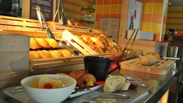 A breakfast counter with pastries, a bowl of fruit, a black mug, and condiments. - ibis Loriol Le Pouzin (Le Pouzin)