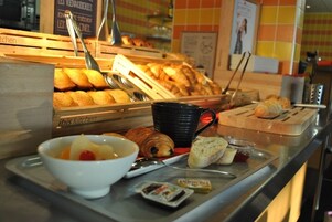 Una barra de desayuno con pasteles, un bol de fruta, una taza negra y condimentos.