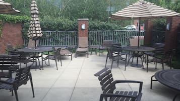 Un área de patio al aire libre con varias mesas y sillas, rodeada por un muro de ladrillo y follaje.