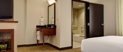 A hotel room with a bed, a TV, a bathroom with a shower, and a minibar.