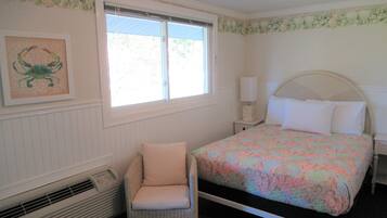 A bedroom with a bed, a chair, a nightstand, a window, and a wall-mounted heater.