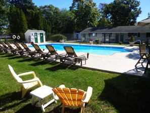 A swimming pool with lounge chairs and a small building, surrounded by grass and trees.
