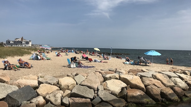A beach with people sunbathing, umbrellas, and a house in the background.