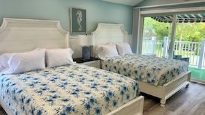 A bedroom with two beds, a nightstand, a lamp, and a seahorse artwork on the wall.