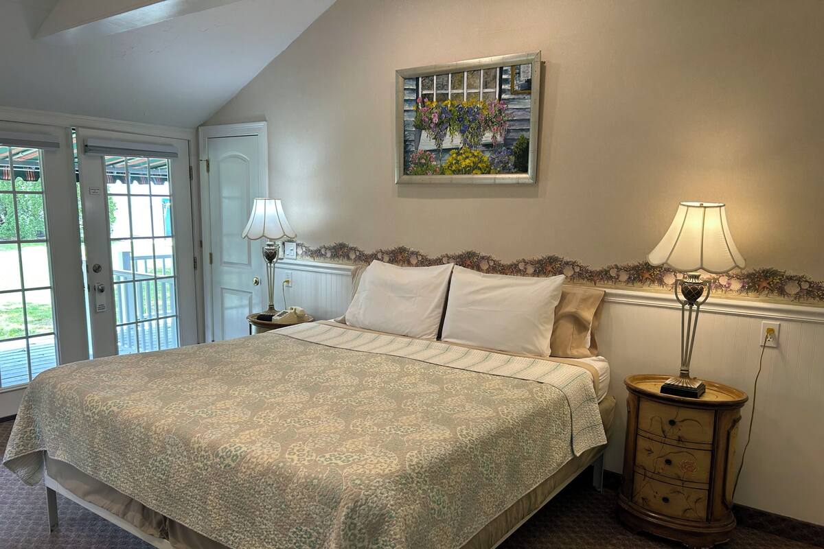 Une chambre avec un grand lit, deux lampes de chevet, une commode et un tableau au mur.